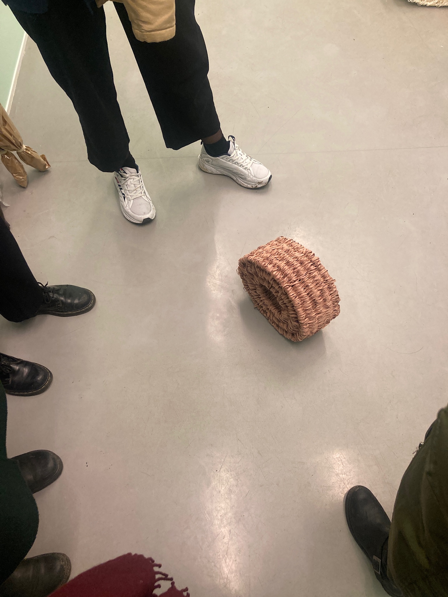 Pink woven paperyarn sculpture on a gray concrete floor surrounded by visitors feet. 