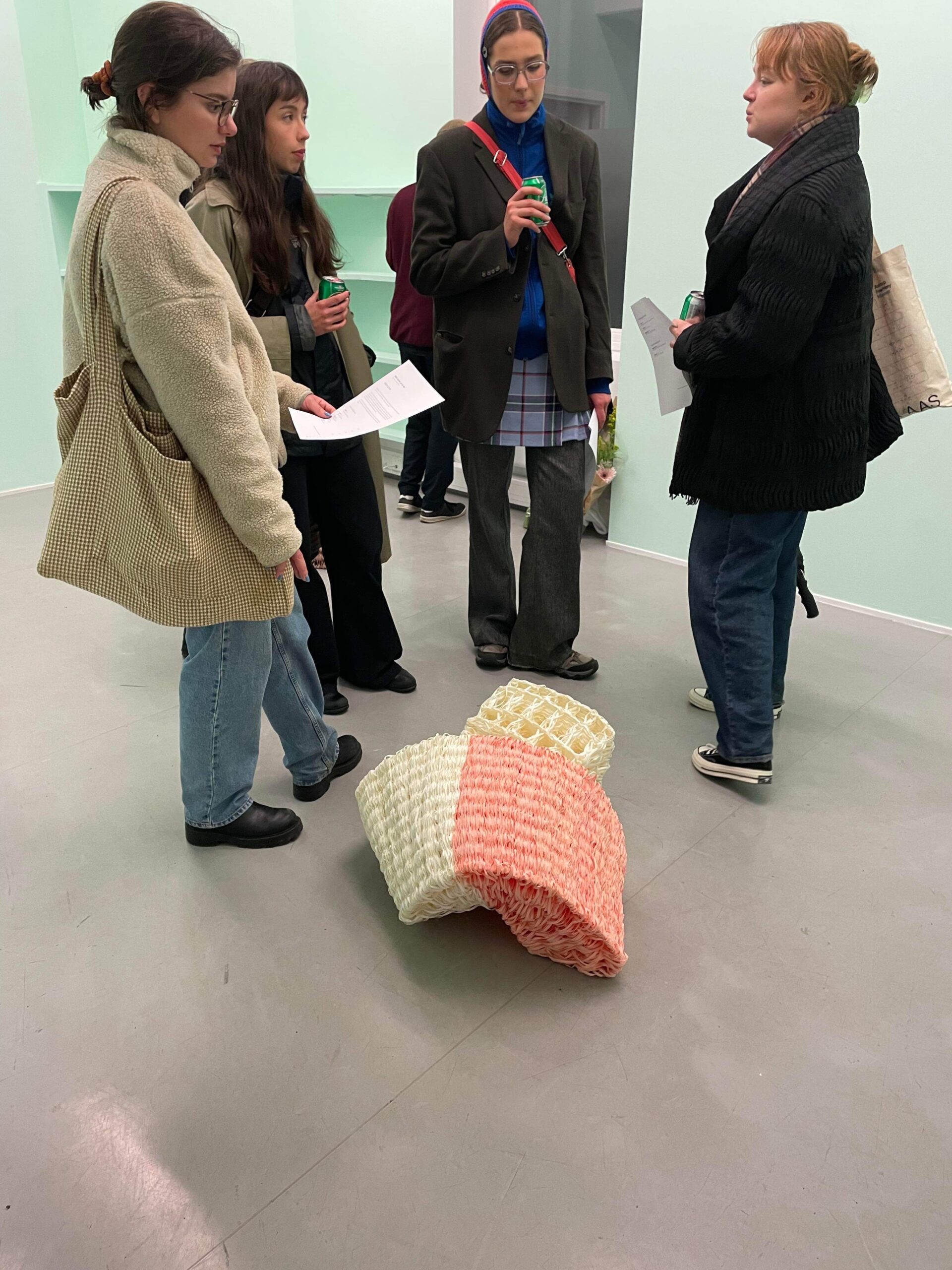 Visitors of a vernissage standing around and watching a the white and pink sculpture "Curl" by Emilia Elfvik.