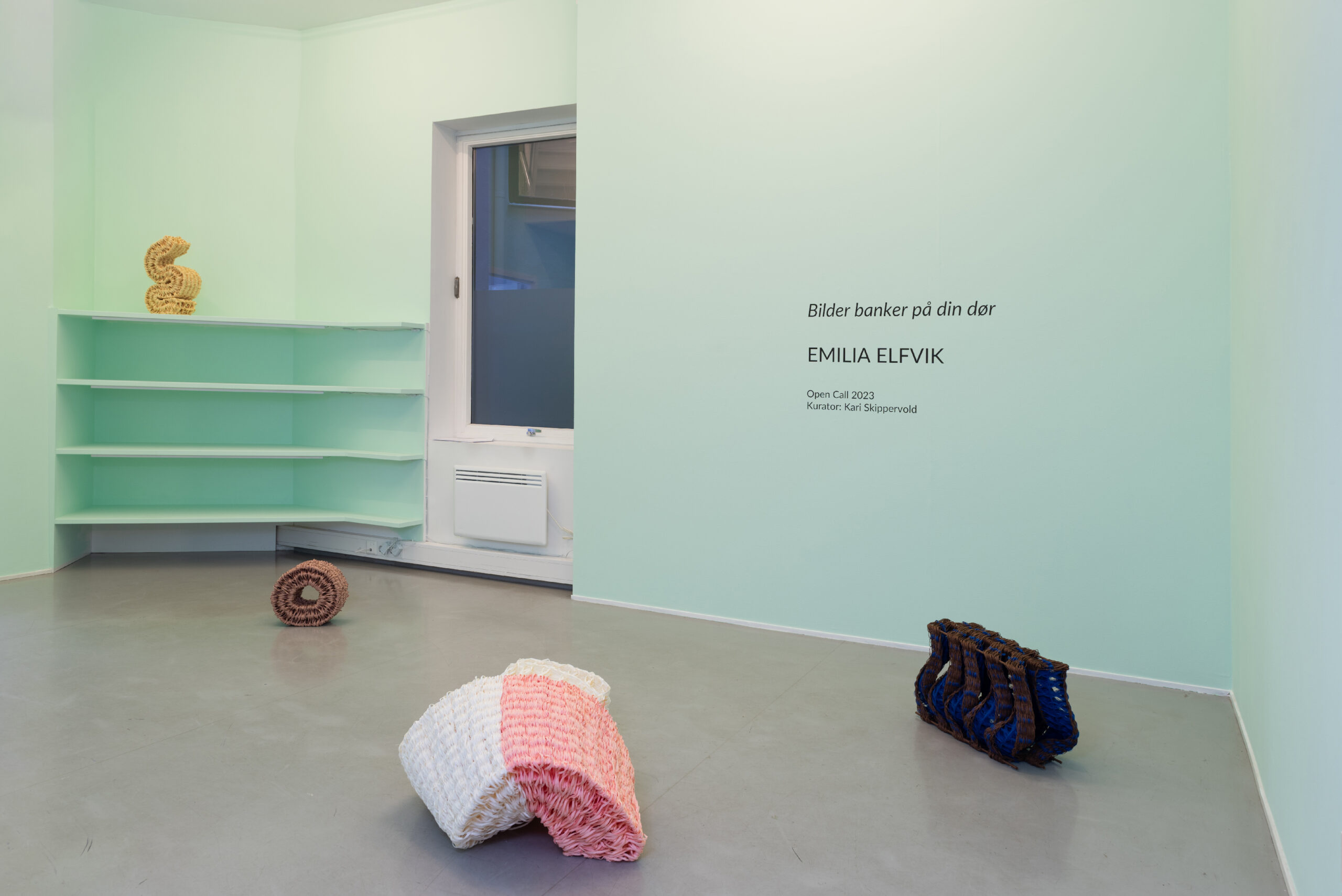 Four woven textile sculptures placed in a turquoise gallery space with grey concrete floor. 